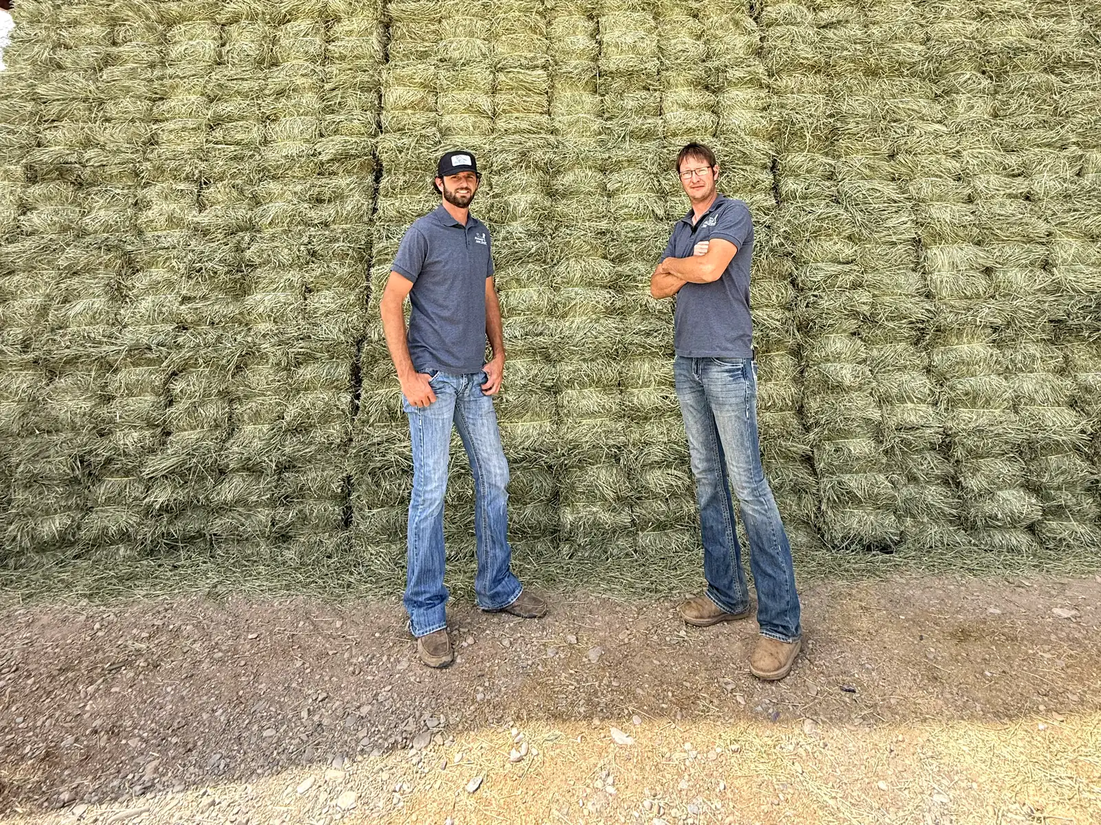 Delmar and Trennis Ropp, owners of Farmers Direct Hay and Feed, standing in front of a stacked wall of hay bales